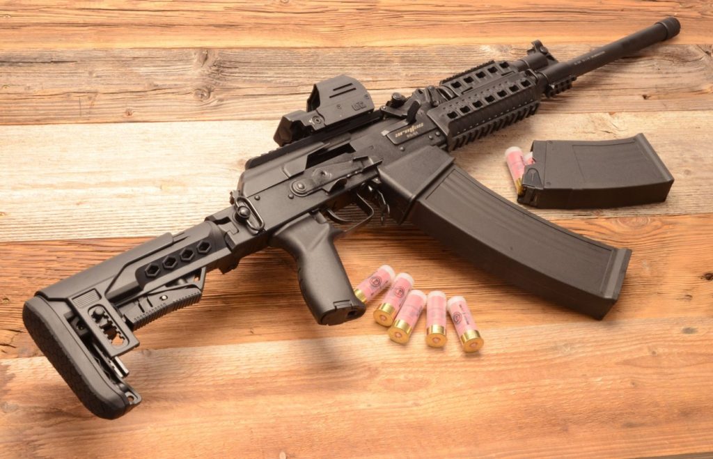A semi-automatic shotgun on a weooden table with clip removed and displayed