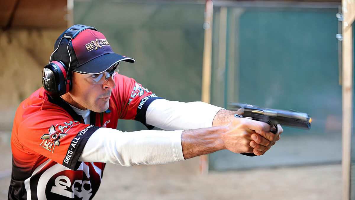 A man with ear protection firing a gun - side view