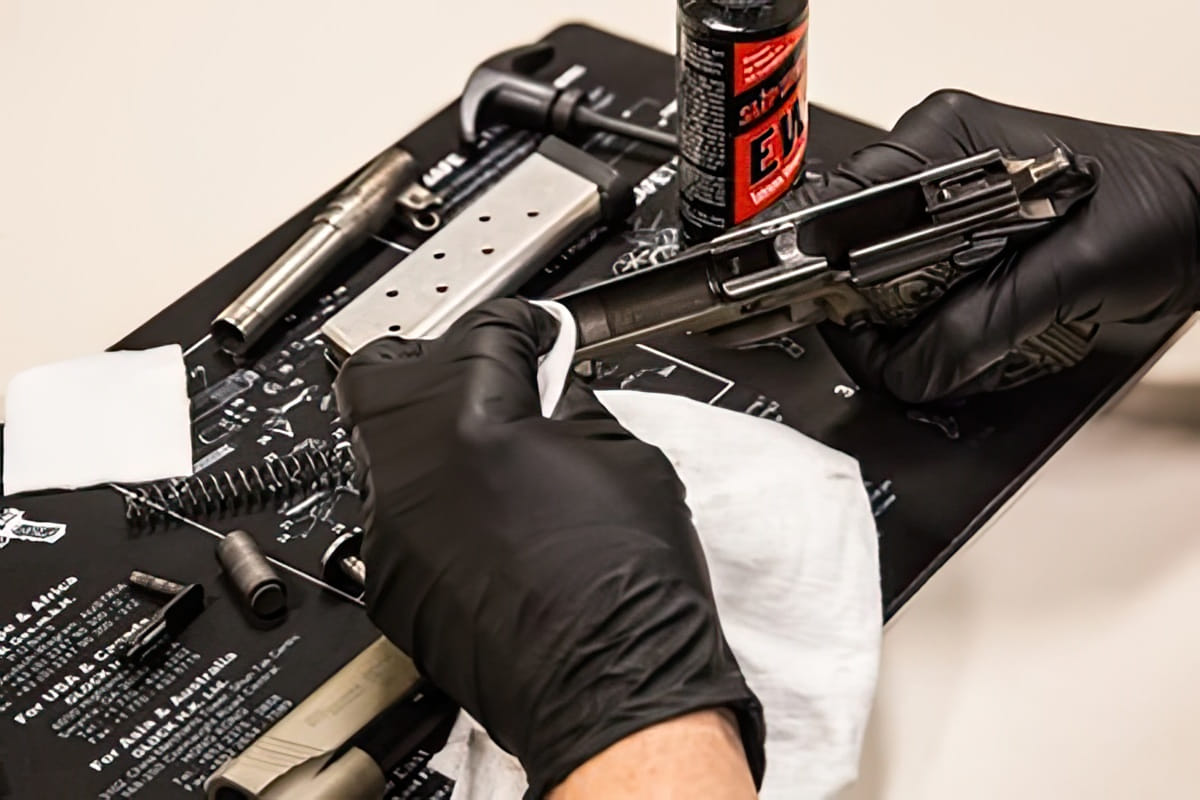 A Person Wearing Black Gloves Is Cleaning A Disassembled Handgun On A Schematic Gun Cleaning Mat